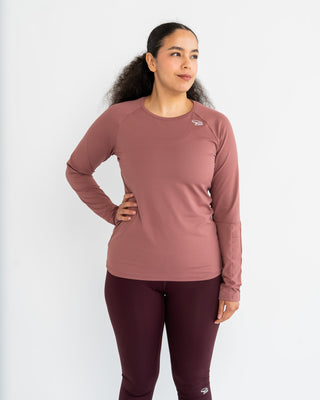 Woman wearing a rosy brown long-sleeve top and raisin red leggings on a white background