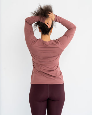 Person wearing a pink long-sleeve top and maroon leggings against a white background