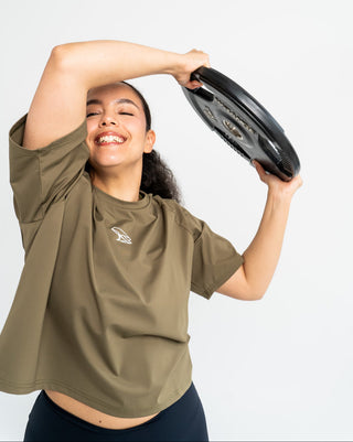 Woman holding a black disc against a white background and wearing Népra Malia Crop T-shirt in pesto green
