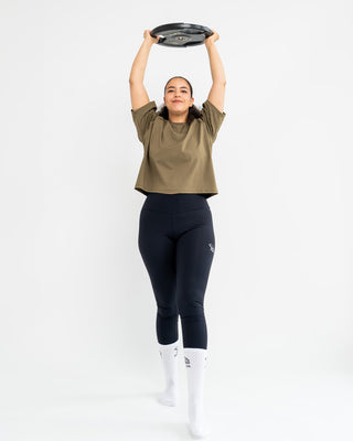 Person lifting a weight plate above their head on a white background and wearing Népra activewear