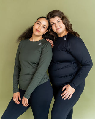 Two women wearing matching long-sleeve shirts and leggings against a green background