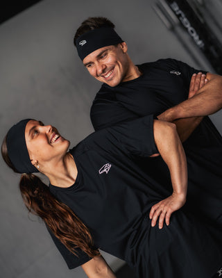 Two people wearing black athletic outfits with a Népra logo, standing close together against a neutral background.