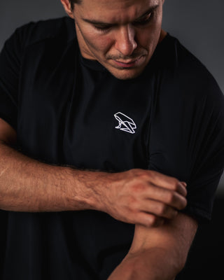 Man wearing a black Népra t-shirt with a white logo on a dark background